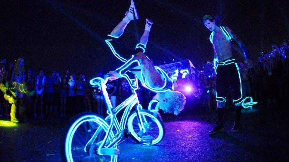 Blake Hicks inverted over the EL-wire bike with a festival crowd around him