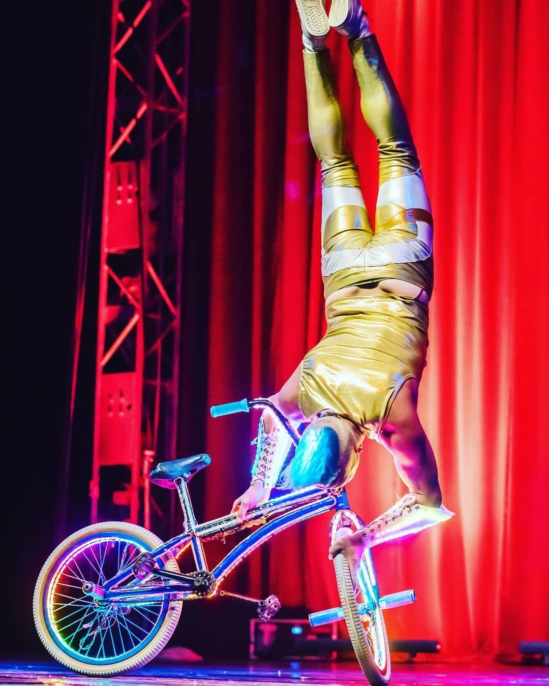 Blake Hicks handstand on the LED bike on a red-curtain stage