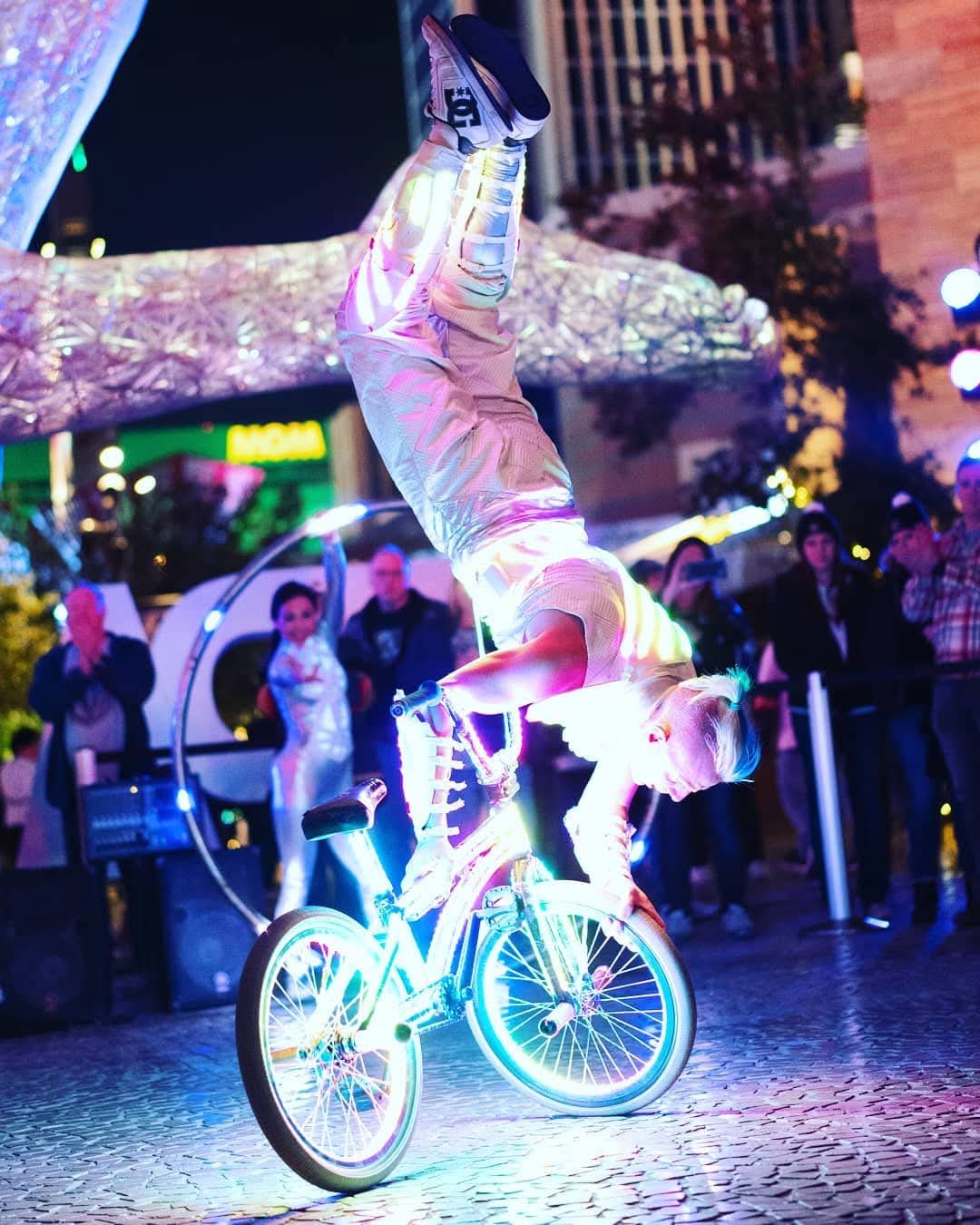 Blake Hicks in a handstand on the glowing LED bike in front of a crowd at The Park, Las Vegas