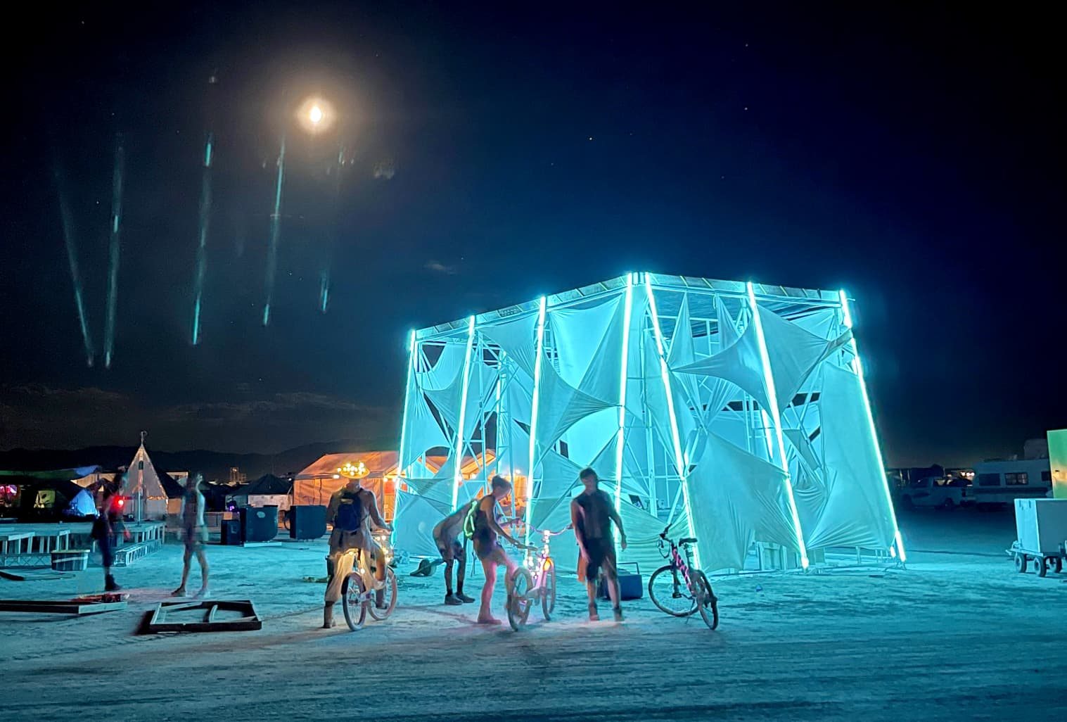 Fabric-draped cube structure outlined in cyan LED bars at night on the playa