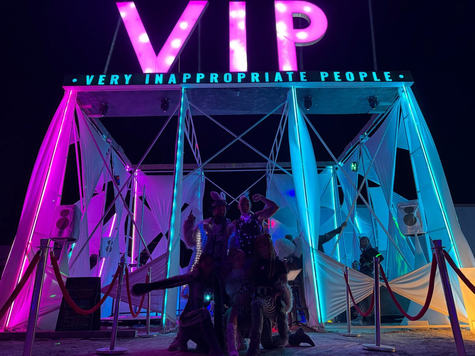 VIP camp entrance lit with pink and cyan LED columns and a marquee sign at Burning Man
