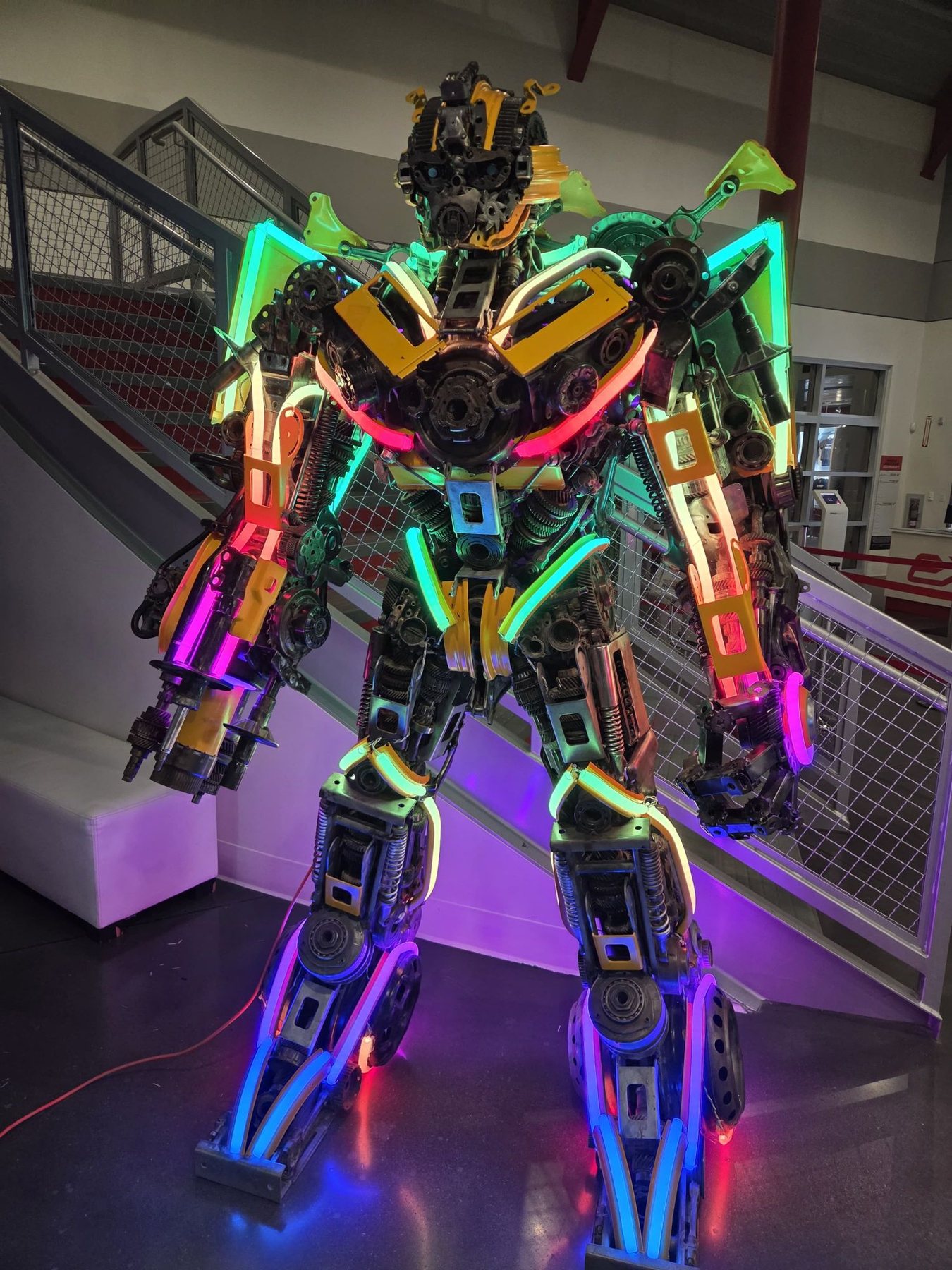 Life-size scrap-metal robot sculpture outlined in rainbow LED neon