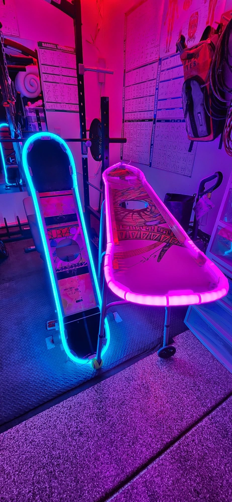 Two painted snowboards edged in cyan and pink LED neon, one standing and one laid flat