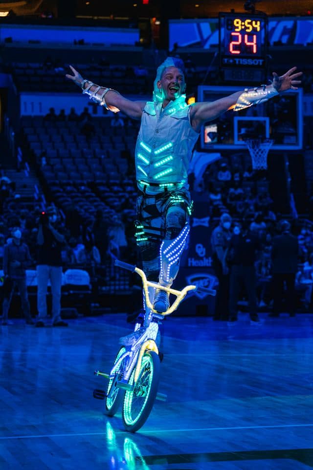 Blake Hicks balancing on the LED Bike with arms wide at an NBA arena
